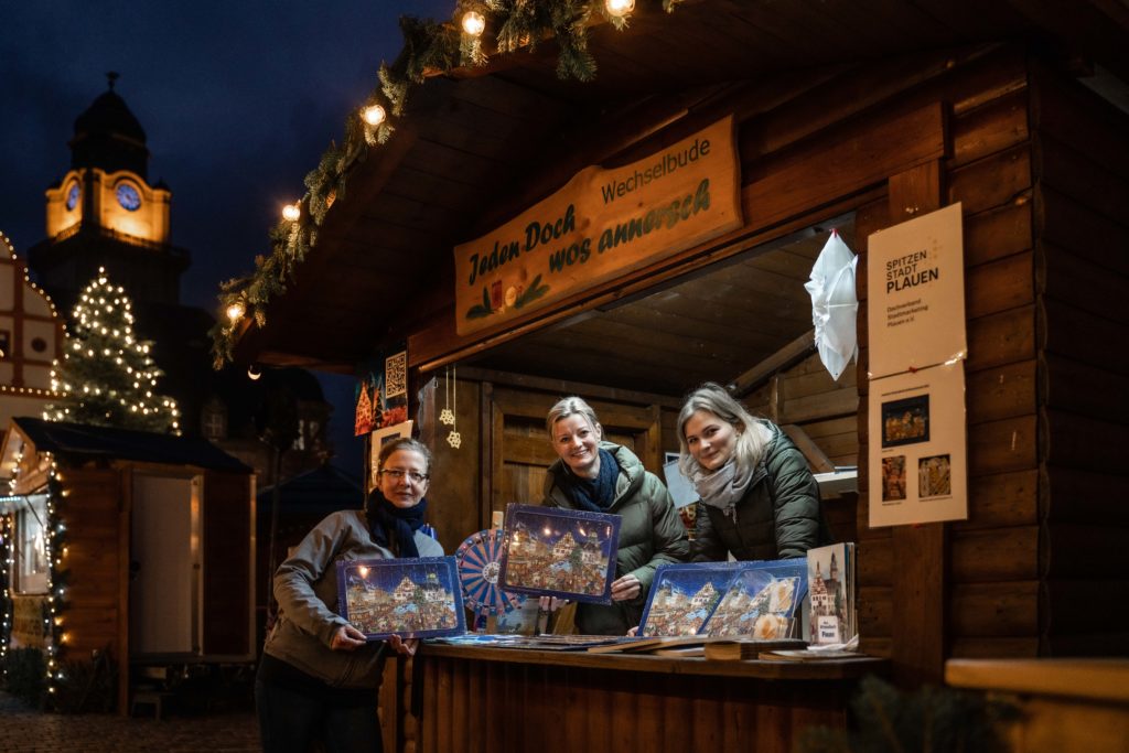 Steffi-Müller-Klug, Sophie Gürtler und Christina Schmidt vom Dachverband Stadtmarketing Plauen e.V. mit dem Wimmel-Puzzle in der Wechselhütte auf dem Plauener Weihnachtsmarkt. Foto: Stephan Roßner- Winkel und Blick Fotografie 