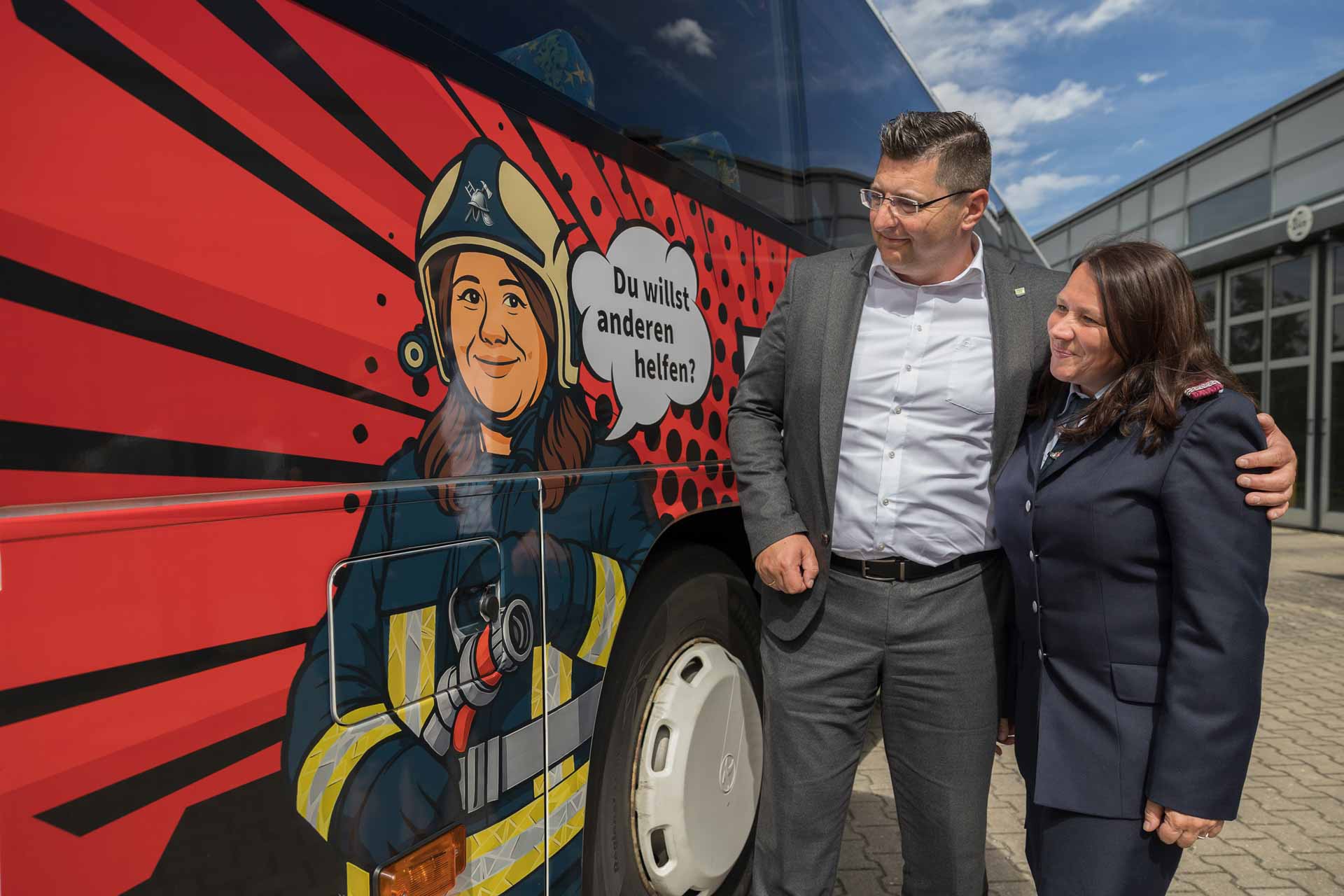 Vorbild trifft Comic: Feuerwehrfrau Sandra Neubert und Landrat Thomas Hennig an einem der beiden neuen Kampagnenbusse © Foto: Landratsamt Vogtlandkreis/David Rötzschke